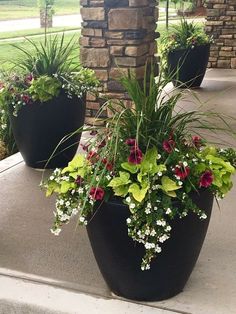 three large black planters with flowers and greenery in them on the front porch