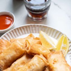 a white plate topped with fried food next to a cup of tea and lemon wedges