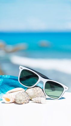 a pair of sunglasses and seashell on the beach