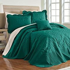 a bed with green comforter and pillows on top of wooden floor next to window