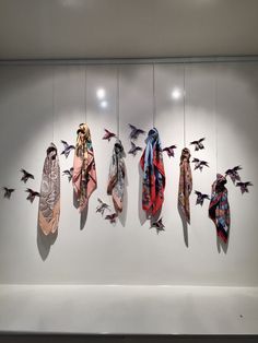 several scarves hanging on the wall in front of a display case with birds flying around them