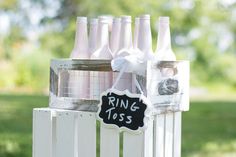 a bunch of wine bottles sitting on top of a white fence with a sign that says ring toss