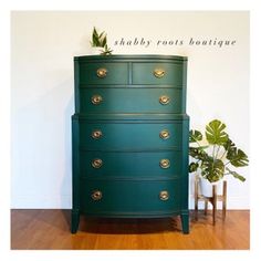 a green chest of drawers sitting on top of a wooden floor next to a potted plant