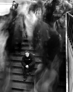 a man sitting on some stairs with his head down and people walking up behind him