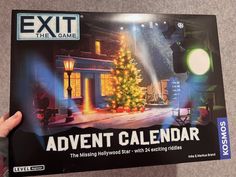 a person holding up an exit the game calendar with a christmas tree in front of it