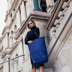 a woman is standing on the steps holding a blue bag and looking at the camera