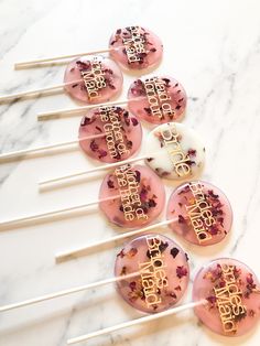 pink cake pops with happy birthday written on them sitting on a marble counter top next to some chopsticks