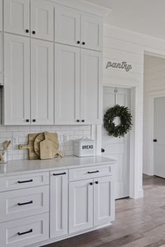 a kitchen with white cabinets and wood flooring is pictured in this image, there are wreaths on the wall