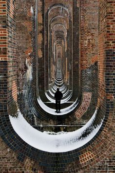 a man is standing in the middle of a brick tunnel with snow on the ground