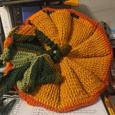 a knitted pumpkin sitting on top of a table next to a spiral notebook and pen