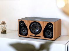 a wooden speaker sitting on top of a white table next to a glass bottle and vase