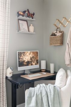 a desk with a computer on top of it next to a white chair and window