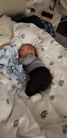 a baby sleeping on top of a bed next to pillows and blankets with blue flowers