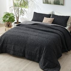 a bedroom with a large bed covered in black linens and pillows, next to a potted plant