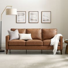 a living room with a brown leather couch and two pictures on the wall above it