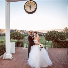 a bride and groom pose for a photo under a clock at their wedding reception in front of an outdoor gazebo