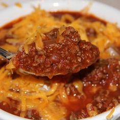 a white bowl filled with chili and cheese covered ground beef in a tomato based sauce