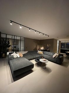 a living room with couches, tables and lights on the ceiling in front of windows