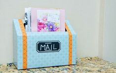 a blue mailbox with flowers in it sitting on a counter next to a wall