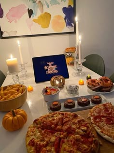 two pizzas sitting on top of a table next to plates of cupcakes