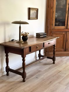 a wooden table with two drawers and a lamp on it next to a bookcase