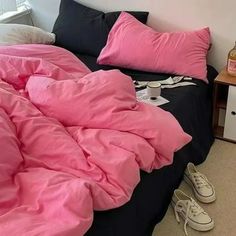 there is a bed with pink sheets and shoes on the floor in front of it