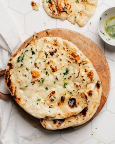 two flat breads are sitting on a wooden board next to small bowls and sauces