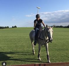 a woman riding on the back of a white horse across a lush green field with a baseball bat in her hand