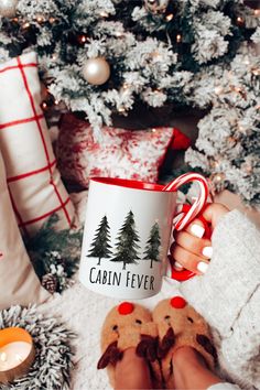 a person holding a coffee mug in front of a christmas tree with their feet up