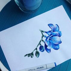 a blue flower is drawn on a piece of paper next to a pen and watercolor pencil