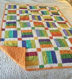 a multicolored quilt is laying on top of a white bedspread with an orange edge