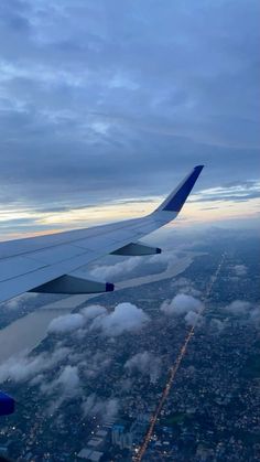 the wing of an airplane as it flies through the sky with clouds and buildings below