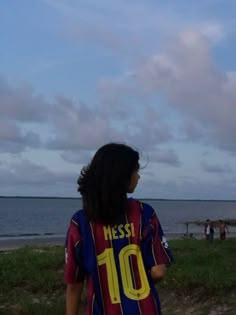 a woman standing on top of a lush green field next to the ocean