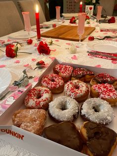 a box filled with donuts sitting on top of a table next to two candles