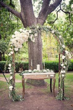 an outdoor ceremony setup with flowers and greenery on the table in front of a tree