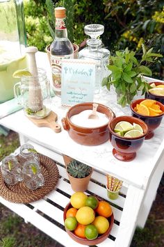 an outdoor table with drinks and fruit on it, including lemons, oranges, limeade