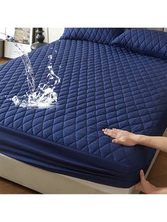 someone is pointing at the water on top of a bed with a blue quilted cover