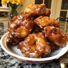 a bowl filled with glazed donuts sitting on top of a counter next to a vase