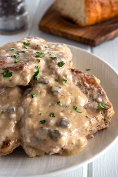 two meat patties covered in gravy on a white plate next to bread