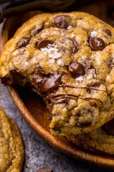 two chocolate chip cookies on a wooden plate with one broken in half and the other partially eaten