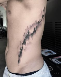 a man's lower back with trees and mountains tattoo on his left side ribcage