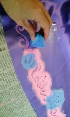 someone is using a sponge to paint the letters on a piece of purple paper with pink and blue icing