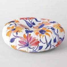 an orange, blue and pink flower pattern on a white background floor pillow sitting on top of a table