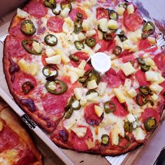 a pizza with pepperoni, pineapple and green peppers in a box next to another pizza