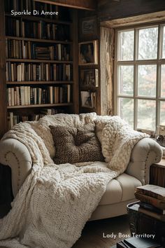 a white couch sitting in front of a book shelf filled with lots of books next to a window