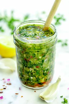 a jar filled with pesto sauce next to lemon wedges and chopped parsley