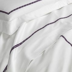 an unmade bed with white sheets and purple trim