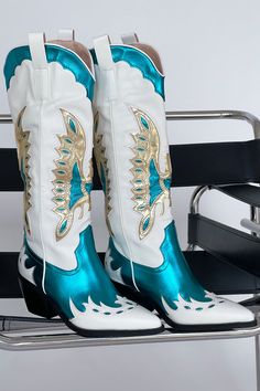 The cowgirl boots of your dreams just landed! The Azalea Wang Apolline Green Metallic Western Boot is a knee-high statement cowboy boot. Step out in style with this high-impact embroidered western boot. Featuring a white body with teal and gold metallic overlay details, and a black sole. Pair these boots with a cute mini dress for the perfect main character energy look! Details: black block heel closed pointed toe structured upper slip on design western inspired embroidery side pull tabs synthet Unique Cowgirl Boots, Metallic Western Boots, Country Costume, Country Costumes, Metallic Overlay, Mode Country, Bota Country, Gold Boots, Metallic Boots