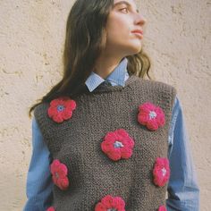 a woman standing in front of a wall wearing a sweater with crocheted flowers on it