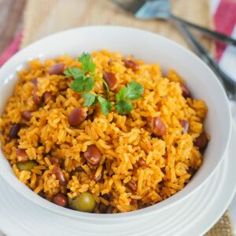 a white bowl filled with rice and beans on top of a table next to utensils